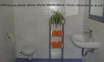 A modern bathroom with bright tiles. Orange towels are on a shelf and a plant adds accents.