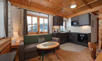 A cozy living and dining room with a wooden ceiling and large windows. The modern kitchen is well-equipped and offers a beautiful view of the surroundings.
