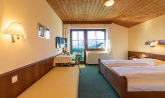 A cozy hotel room with two beds and a table. Large windows offer a view of the mountains.