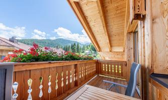 A beautiful balcony with wooden cladding and colorful flowers. In the background, the mountains and the blue sky can be seen.