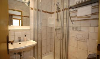 A modern bathroom with a shower cubicle and a sink. The walls are tiled and there are towels and toiletries nearby.