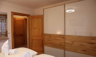 A modern bedroom with a bed and a large, elegant wardrobe. The walls are light, and the furniture is made of wood.