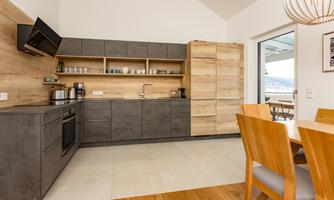 A modern kitchen with dark cabinets and wooden paneling. The dining area with light chairs complements the inviting atmosphere.