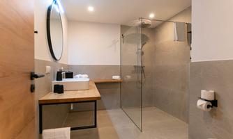 A modern bathroom with a glass shower and a large mirror. The room is brightly and minimally designed.