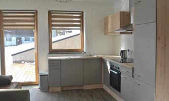 A modern kitchen with gray cabinets and bright wood accents. Large windows bring in plenty of light and offer a view of the terrace.