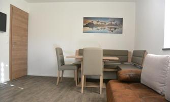 A modern dining room with a table and chairs. A painting of mountains and a lake hangs on the wall.
