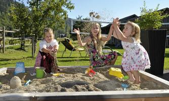 Three children are happily playing in a sandpit. They throw sand into the air and enjoy the sun outdoors.