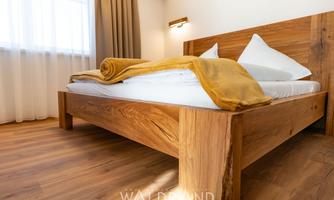 A cozy bedroom with a wooden bed and fresh white bed sheets. A golden blanket is neatly placed over the bed and the light is soft.