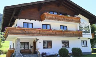 A traditional mountain house with wooden decorations and balconies. Surrounded by green meadows and mountains.