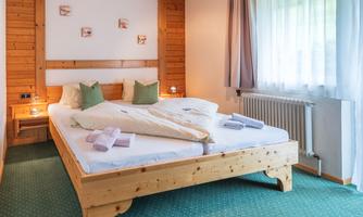 A cozy bedroom with a large double bed and wooden paneling. The atmosphere is bright and inviting, with soft pillows and a green carpet.