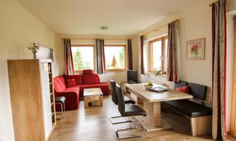 A bright living room with red sofas and a wooden table. Large windows offer views of the outdoors and let in plenty of light.