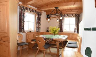 A cozy dining area with wooden paneling and a round table. Large windows provide plenty of light, and there is a bouquet of fresh flowers on the table.