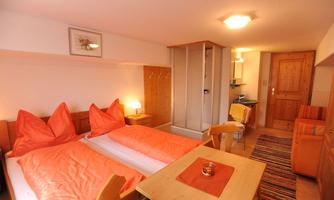 A cozy room with two beds in warm colors and a small seating area. The decor is simple and inviting, perfect for a relaxing stay.