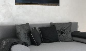 A modern gray sofa with cushions is situated in front of a wall with a built-in television. The room has a bright, minimalist style.