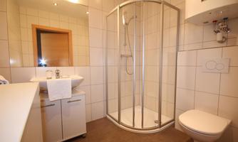 A modern bathroom with a shower, a sink, and a toilet. The walls are tiled with white tiles, and the room feels clean and inviting.