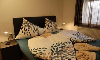 A cozy bedroom with a double bed and elegant bedding. Next to the bed, there is a bedside table with a lamp.