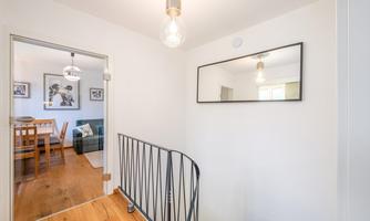 A bright hallway with a curved staircase and a large wall mirror. In the background, you can see a cozy living area with a dining table.