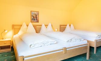 A cozy bedroom with three beds and yellow paint. The decor is simple and inviting, with a bedside table and a piece of artwork on the wall.