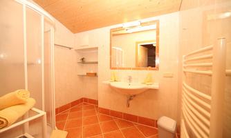 A modern bathroom with a shower and a sink. The walls are brightly tiled, and there are towels in soft colors.