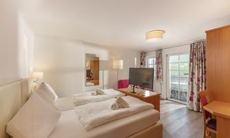 A bright room with two single beds and a television. Large windows provide access to a balcony with an outdoor view.