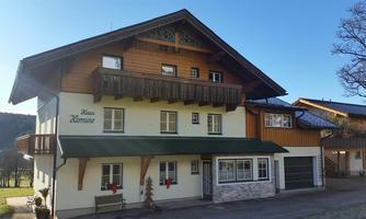 A traditional wooden-clad house with a beautiful balcony. The facade is bright and friendly, surrounded by a rural setting.