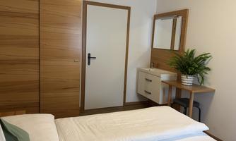 A simple bedroom with two single beds. On the wall, there is a mirror, a small table, and a green plant.