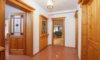 A bright hallway with wooden paneling and doors. In the background, another room is visible.