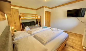A modern bedroom with a double bed and a bunk bed. The walls are bright and a television hangs on the wall.