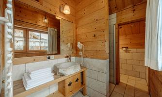 A rustic bathroom with wooden walls and a large mirror. Fresh towels are ready on the wooden bench.