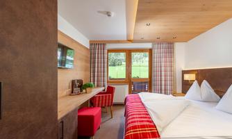 A modern hotel room with two beds and wooden elements. Large windows offer a view of the green landscape.