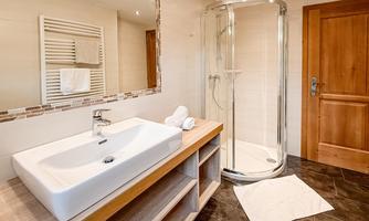 A modern bathroom with a shower and a white ceramic sink. Wooden shelves and soft lighting create an inviting atmosphere.