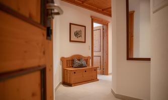 An inviting hallway with wooden details and a wooden bench. The walls are bright, and there is a door leading to another room.