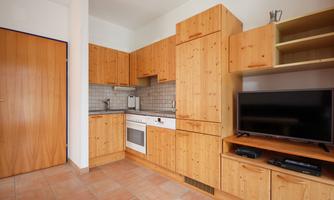 A modern kitchen with wooden cabinets and a television. The kitchen is bright and well-equipped.