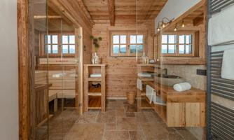 A modern bathroom with wood paneling and plenty of natural light. There is a separate shower area and a wooden sink.