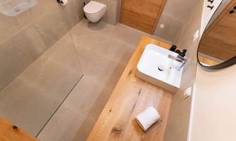 A modern bathroom with a large wooden shelf and an elegant sink. The walls are light, and the shower is integrated into a glass wall.