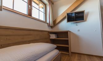 A cozy bedroom with a wooden bed and a TV on the wall.  
Bright windows provide plenty of daylight.