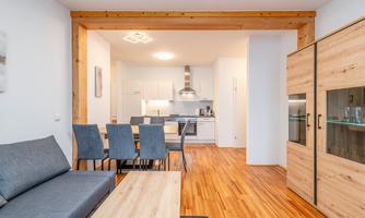 A modern apartment with a cozy living room and an open kitchen. The wooden floor and the furniture create a warm atmosphere.