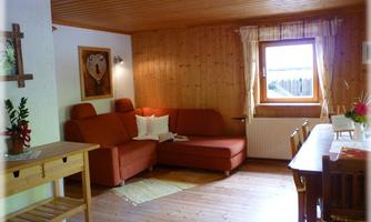 A cozy living room with a red sofa and a wooden plank floor. Natural light falls on the dining table and the decoration through the window.