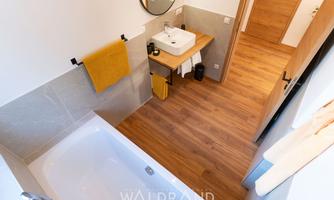 A modern bathroom with a bathtub and a sink. Wooden floor and soft colors create an inviting atmosphere.
