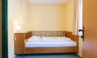A simple bedroom with a single bed and a nightstand. The walls are light yellow and there is soft lighting.