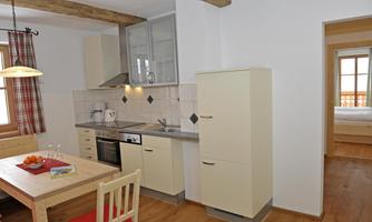 A modern kitchen with a bright wooden floor and minimalist furniture. The dining area is cozily furnished and provides seating for several people.