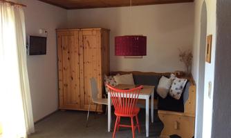 A cozy dining area with a wooden cabinet and a seating corner. The table is decorated with a colorful chair and cushions.