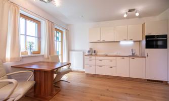 Modern kitchen with bright furniture and large windows. A wooden dining table with two chairs complements the space.