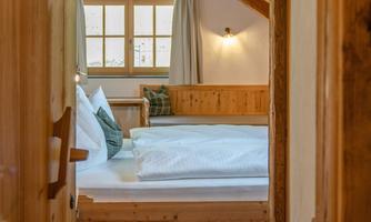 A cozy room with a wooden ceiling and a large bed. Through the door, you can see windows with plenty of natural light.