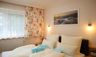 A cozy bedroom with two beds and many pillows. A picture of a coastal landscape hangs on the wall.
