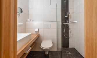 A modern bathroom with a shower, a sink, and a toilet. The walls are brightly tiled and there are wood panelings.