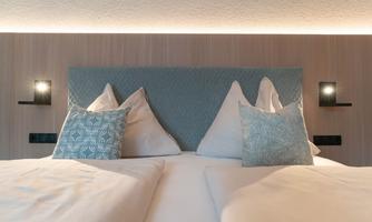 A cozy double bed with soft pillows and a modern headboard. The soft lighting creates a relaxed atmosphere.