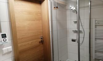 A modern bathroom with a glass shower and a wooden door. The walls are brightly tiled and there is a towel warmer.