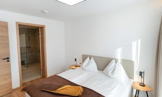 A bright bedroom with a large bed and two pillows. The decor is modern and welcoming, with a friendly color scheme.