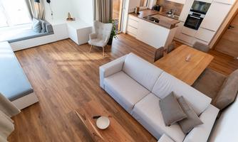 A modern living room with a light wooden floor and an open kitchen. The decor is stylish and minimalist, featuring a cozy sofa and a dining table.
